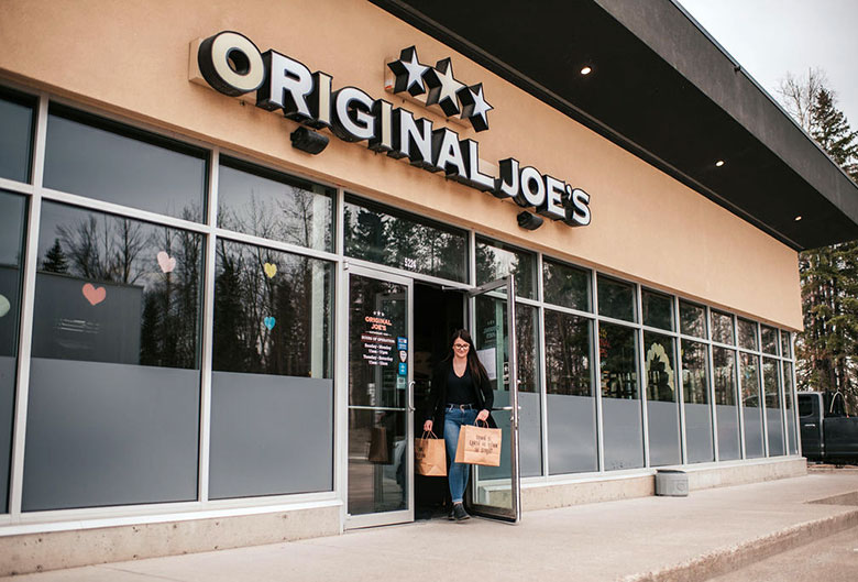 Woman leaving Original Joe's with take out food.