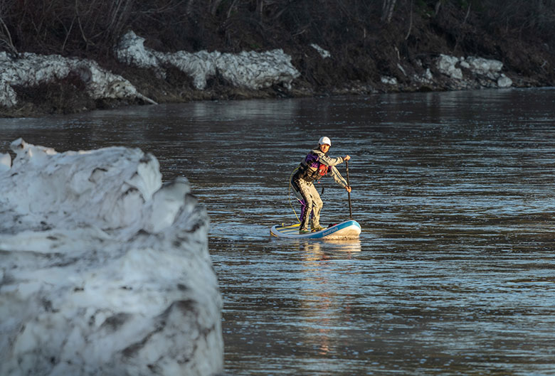 Woman paddle boarding down river.